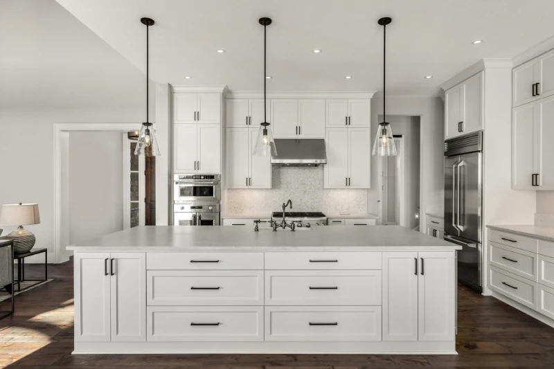 Texas Down Payment Assistance 1 Modern white kitchen with large island featuring drawers, pendant lighting, stainless steel appliances, white cabinets, and dark hardware, set on a wooden floor with a clean, minimalist design.